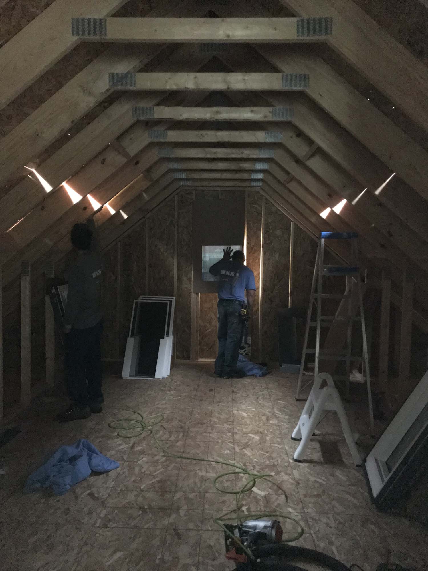 Workers install two large square skylights in an A-frame attic space